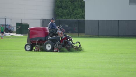 trabajador paisajista corta un campo de fútbol de hierba con una cortadora de césped en el verano durante el día