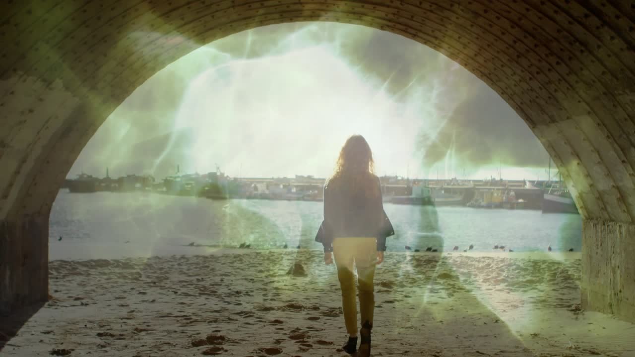 Woman walking through stone arch onto sandy beach as emerging green energy portal animating AR demo