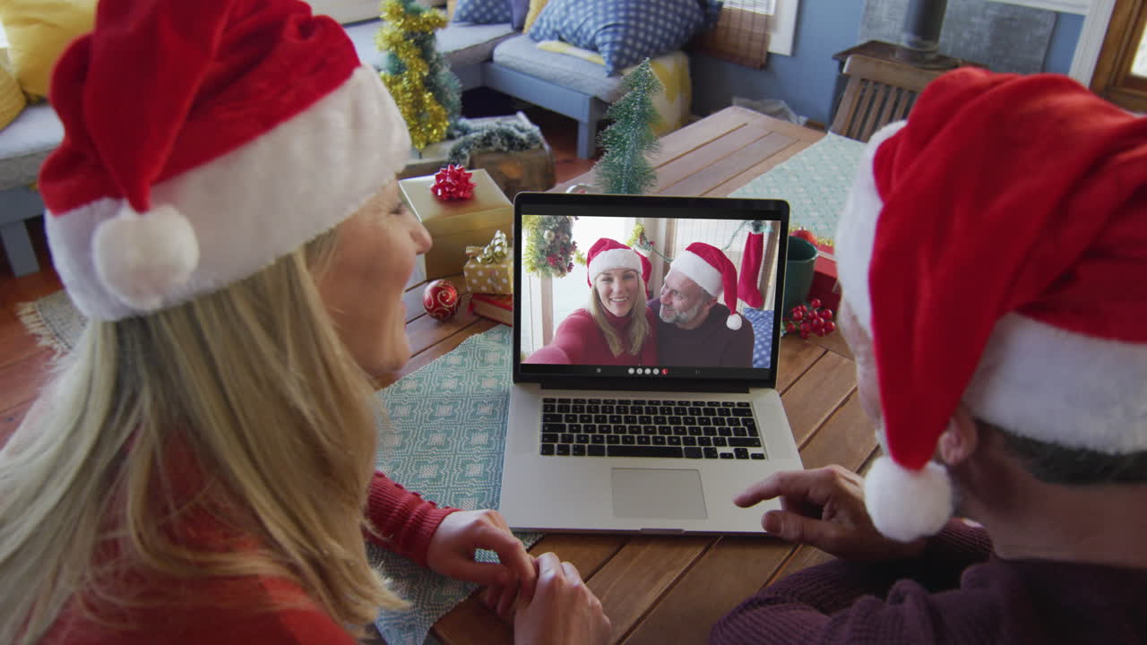pareja caucásica sonriente con sombreros de santa usando una computadora portátil para una videollamada de navidad con la pareja en la pantalla