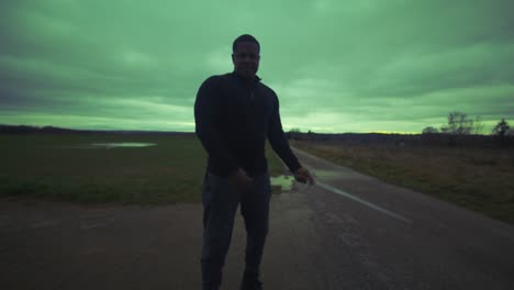 modern black swordsman warrior awaiting battle opponent in open field under green sky, europe, 4k | muscular, intimidating, shadow, figure, blurry, dark clothes, powerful, adjusting stance to slash