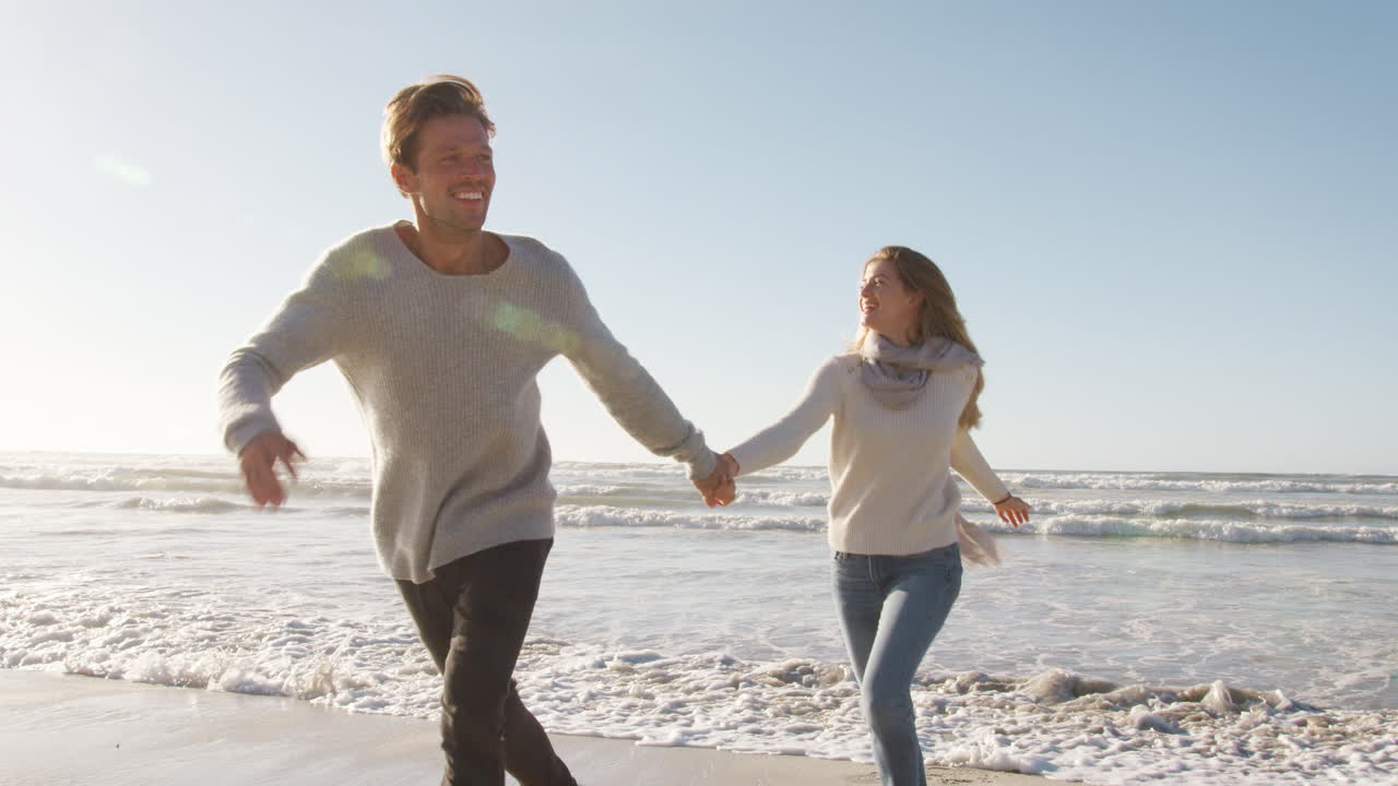 재미 있는 커플 이 함께 겨울 해변 을 따라 달리고 있다