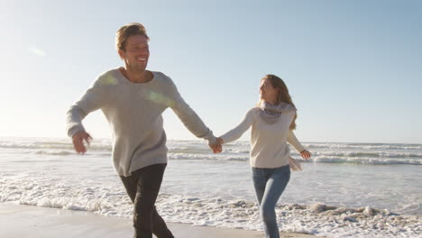 Pareja-Divirtiéndose-Corriendo-Juntos-Por-La-Playa-De-Invierno