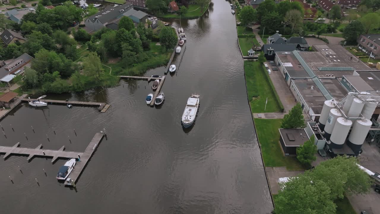 Aerial view of Luxemotor boat leaving dock through calm canal in a peaceful neighborhood in the Netherlands. Zoom out