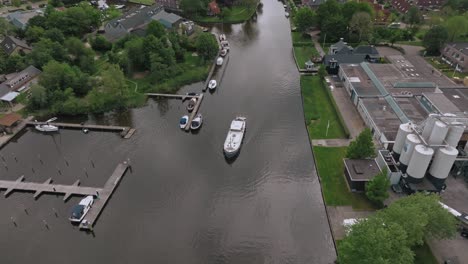 aerial view of luxemotor boat leaving dock through calm canal in a peaceful neighborhood in the netherlands. zoom out