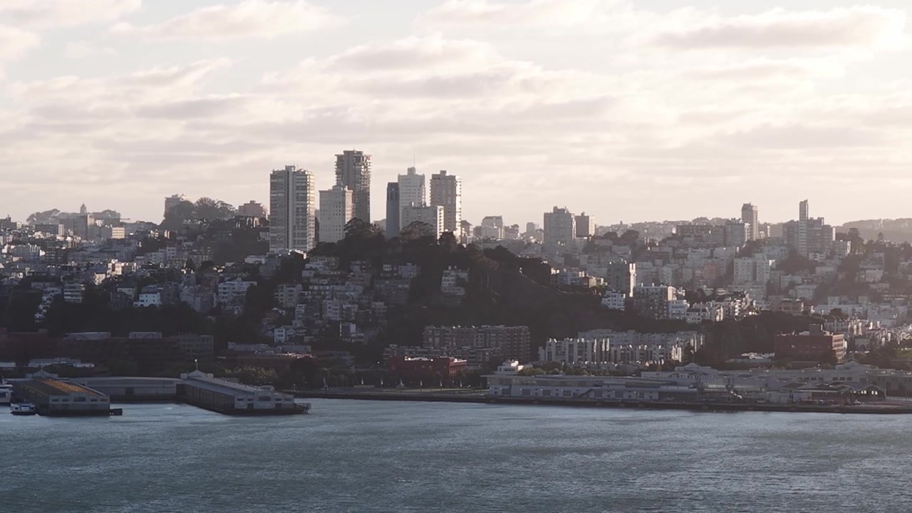 Splendida vista aerea della città di San Francisco dall'altra parte della baia, con la luce calda del sole al tramonto che proietta un bagliore sull'acqua e lo skyline urbano sotto un cielo parzialmente nuvoloso.