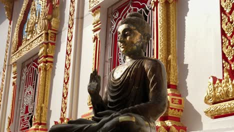 thai protection buddha statue with raised hand sitting outside buddhist temple, thailand