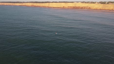 Toma-Aérea-En-órbita-De-Una-Persona-Con-Kayak-Remando-En-El-Amplio-Océano-Atlántico-Frente-A-Los-Acantilados-En-Los-Acantilados-De-Mar-Del-Plata-Durante-La-Hermosa-Puesta-De-Sol