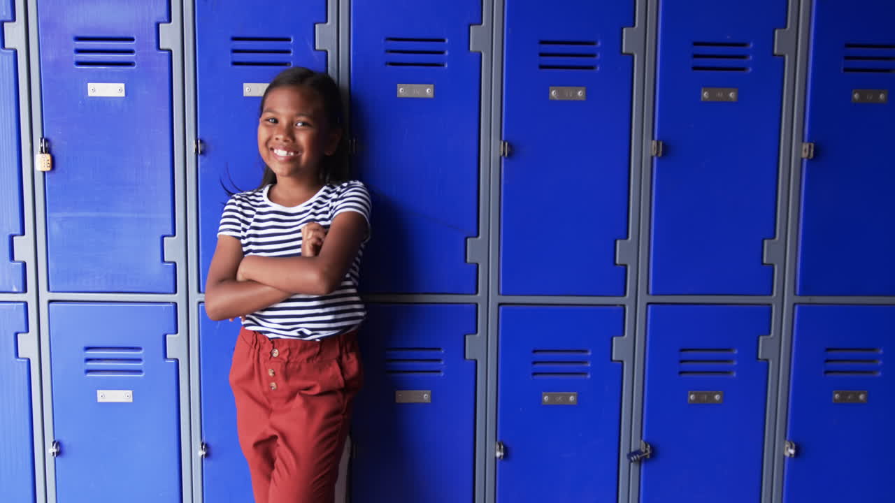 In a school hallway, a young African American girl leans against blue lockers with copy space