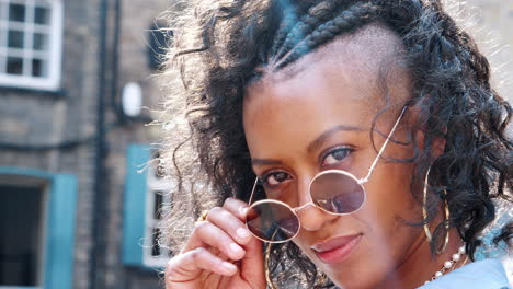 Trendy-young-black-woman-wearing-round-sunglasses-turns-to-look-to-camera,-head-shot,-side-view