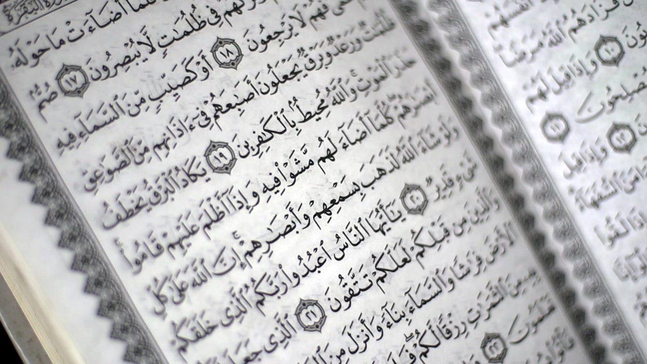 Mani che voltano le pagine del Corano leggendo la sura Al-Baqarah, su sfondo nero, ripresa in primo piano