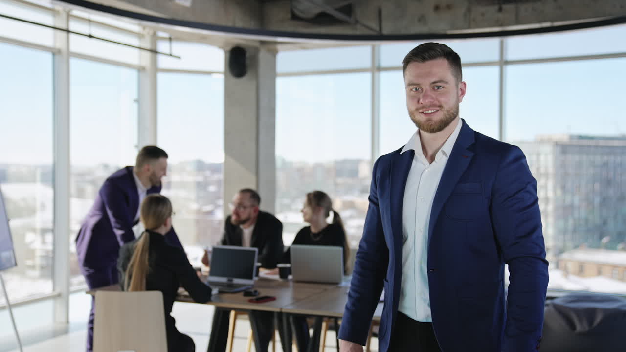 Man in a suit looking in the camera and smiling. Portrait of a young businessman. Business collaboration at the table in the background.