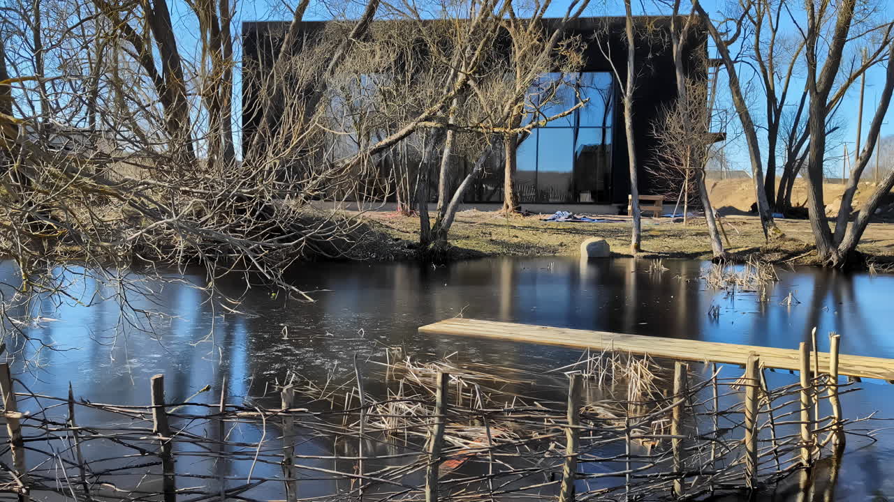 Tranquil Pond with Reflection In Wooden House and Bare Trees on sunny Spring Day