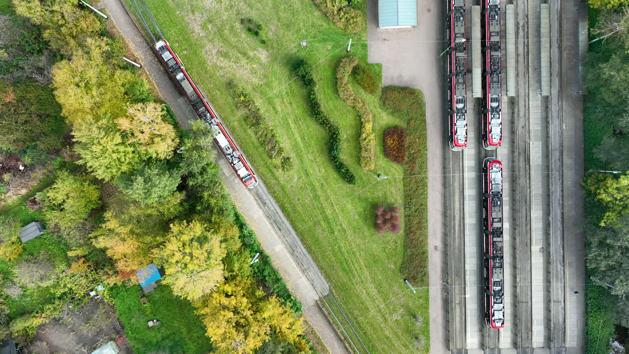 Aerial drone view of red tram moving through green park area and depot in Gdańsk Jelitkowo, Poland
