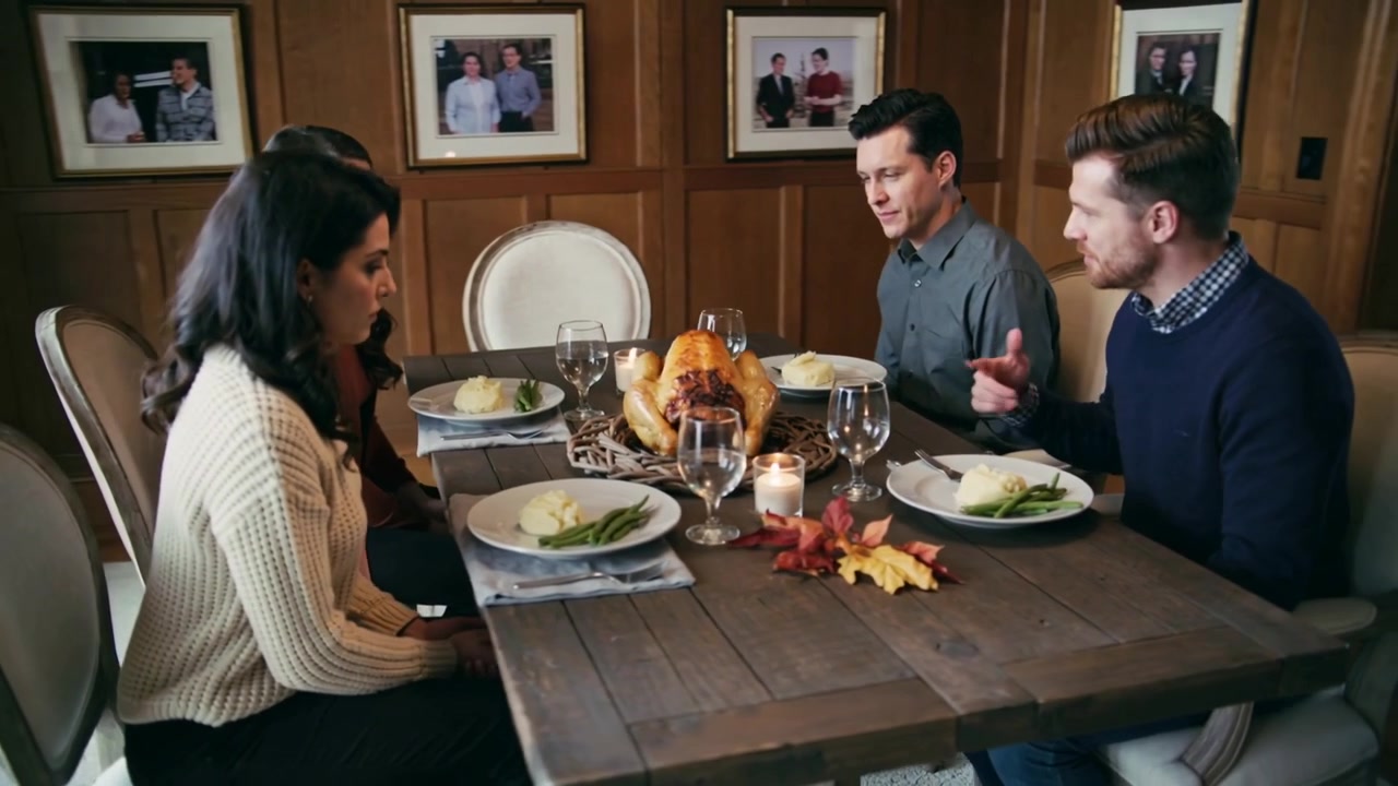 Leaning forward, man in blue sweater initiating brief grace at home dining room with roasted turkey