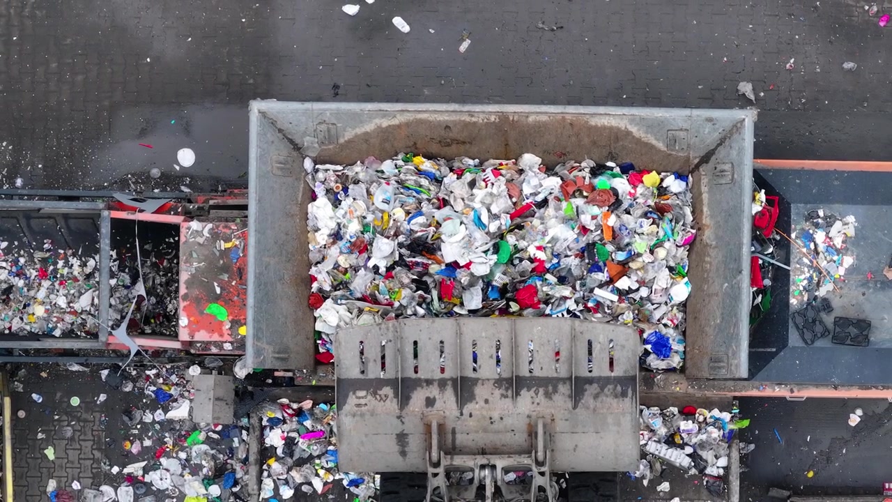 I rifiuti di plastica vengono caricati in un impianto di riciclaggio per la selezione e la lavorazione. I veicoli trasportano materiali plastici per il riciclo. Le operazioni si concentrano sulla riduzione dei rifiuti e sul recupero delle risorse