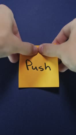 hands posting push sticky note on dark blue wall, emphasizing drive