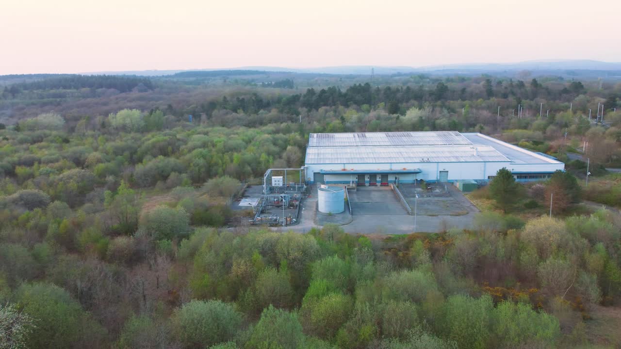 Bredt luftfoto over nedslidt lager med læsseramper omgivet af stort skovlandskab. Industriel infrastruktur omgivet af naturligt miljø. 4K.