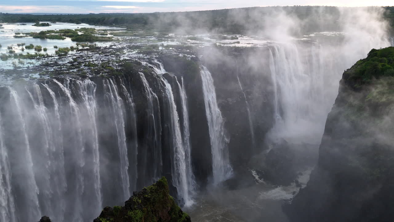 Aerial view of Victoria Falls with powerful waterfall plunging into gorge, mist rising above lush green forest, dramatic natural wonder and iconic travel destination in Africa