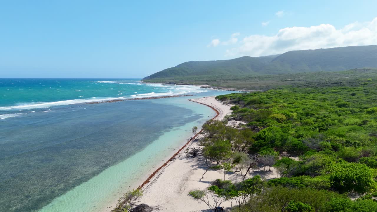 Aerial rising shot of Playa Caobita with clear ocean water and breaking waves. Exotic landscape coastline with green mountain in distance. Sunny day in summer. Wide shot.