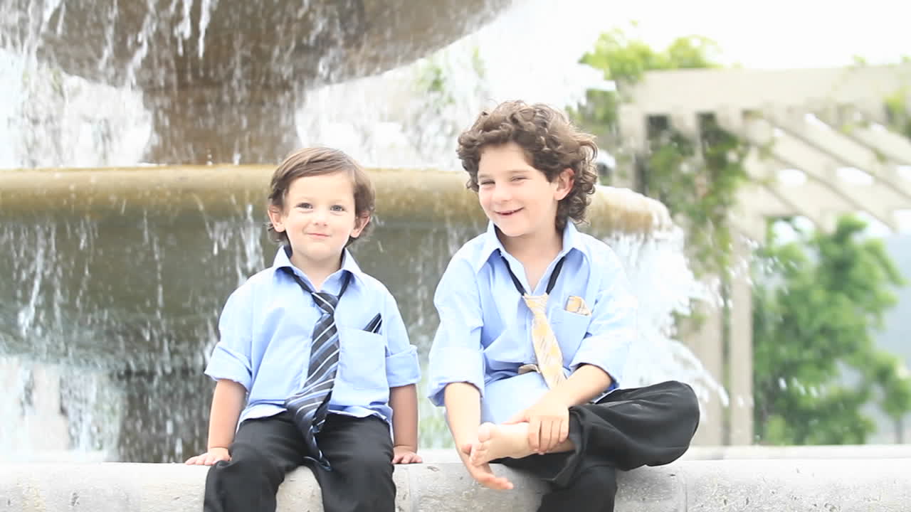 пара мальчиков в формальной одежде играют перед фонтаном