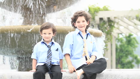 a pair of boys in formal dress play in front of a fountain