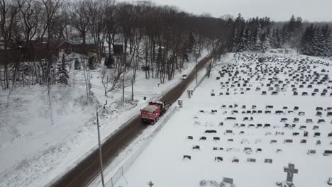 Quitanieves-En-Una-Carretera-Junto-A-Un-Cementerio-Cubierto-De-Nieve