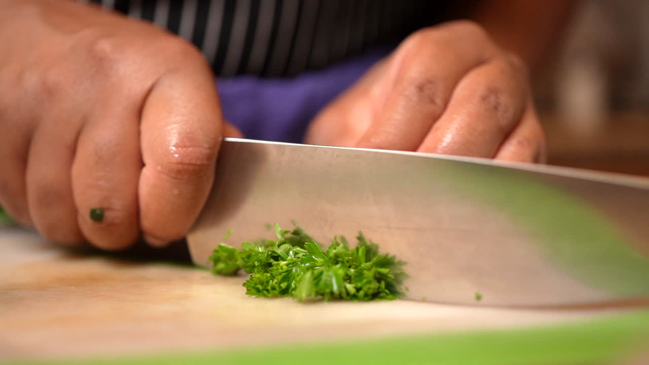 Hands in isolation seen chopping parsley with a kitchen knife in slow motion