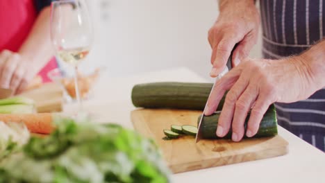 Senior-caucasian-man-chopping-courgette,-preparing-food-in-kitchen-with-friends,-slow-motion