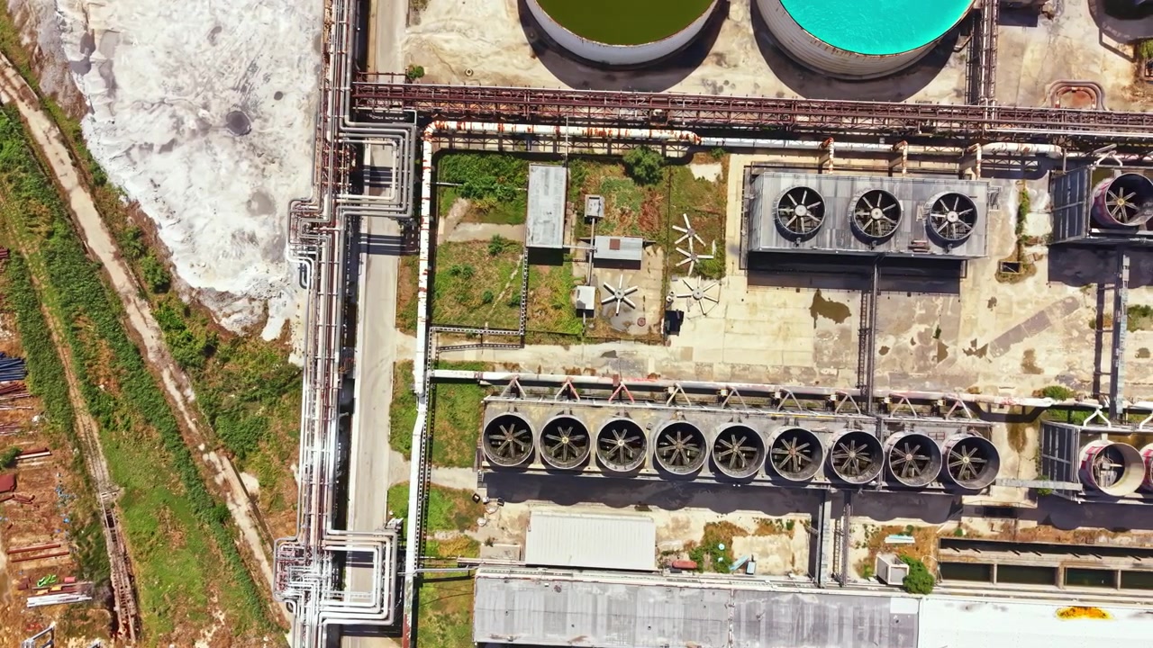 Industrial site with pipelines and storage tanks located near a green area and dirt road