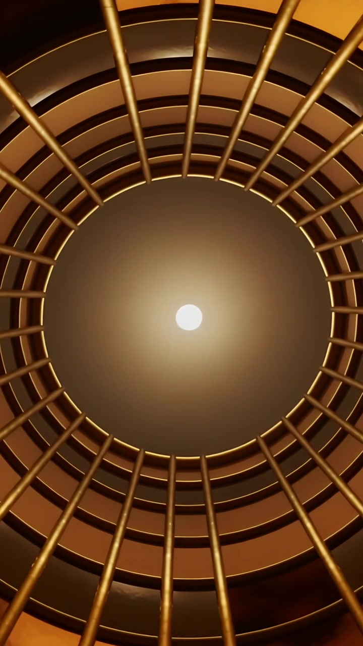 Vertical video: Camera tilting, showing circular fixture in lobby, center light, rings, gold bars