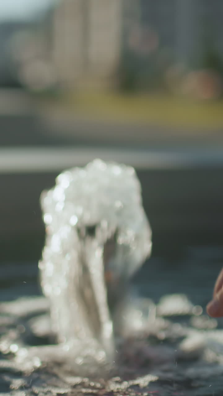 가까운 손으로 은 물 표면 반사, 흐릿한 형상 및 배경으로 분수에서 흐르는 물에 도달합니다.