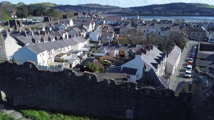 Cottage vacanza gallesi racchiusi tra le mura merlate in pietra del castello di Conwy, vista aerea con movimento ascendente e verso sinistra.