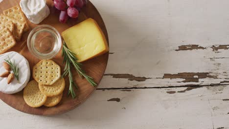 Video-of-cheese,-biscuits,-grapes-and-rosemary-on-wooden-board-and-rustic-table-top-with-copy-space