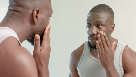 applying facial cream, african american man looking in mirror, focusing on skincare