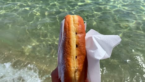 holding a traditional french beignet sold at the beach during summer in cavaière lavandou south of france, famous sweet deep-fried pastry fritter, 4k shot