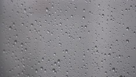 close up of small raindrops on glass window, wet surface background, static shot