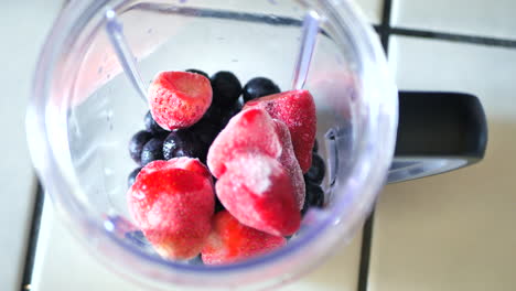 pouring frozen blueberries and strawberries into blender to make smoothie or fitness shake