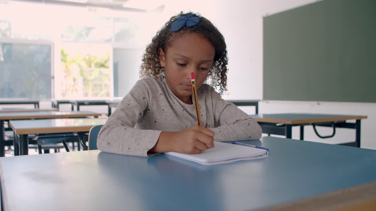 Giovane ragazza multietnica che scrive su un foglio in classe