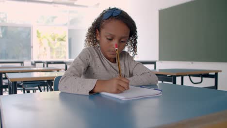 Young-mixed-girl-writing-on-paper-in-classroom