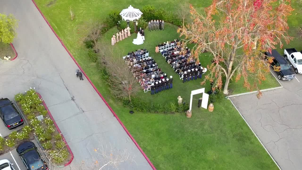 Aerial drone rising shot over a military outdoor wedding with gazebo with the uniformed Navy officers in the back row.