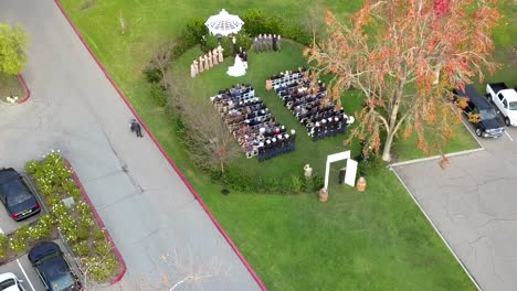aerial drone rising shot over a military outdoor wedding with gazebo with the uniformed navy officers in the back row.