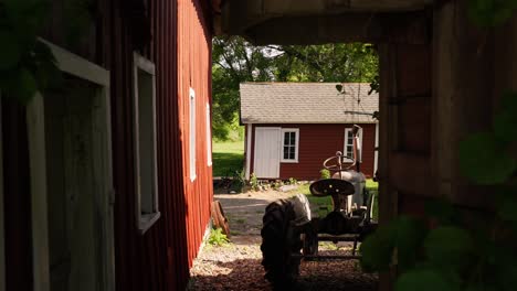 panning-shot-in-between-a-barn-looking-towards-another-barn-with-an-old-tractor-in-the-foreground