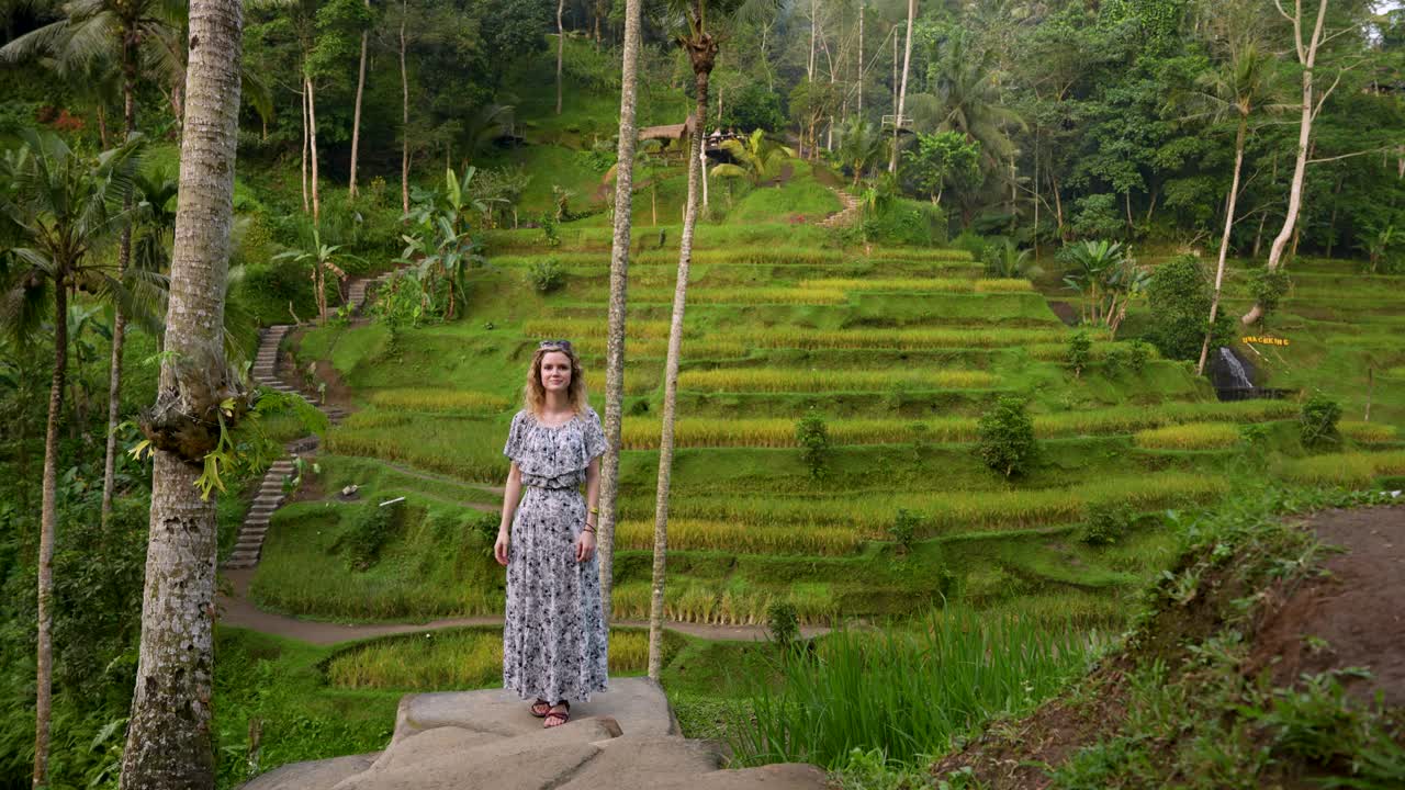 Turista felice in piedi tra le lussureggianti risaie a terrazza di Tegallalang, Bali, circondato dal verde tropicale e dalle palme, immortalando un pacifico momento di viaggio in uno scenario indonesiano pittoresco