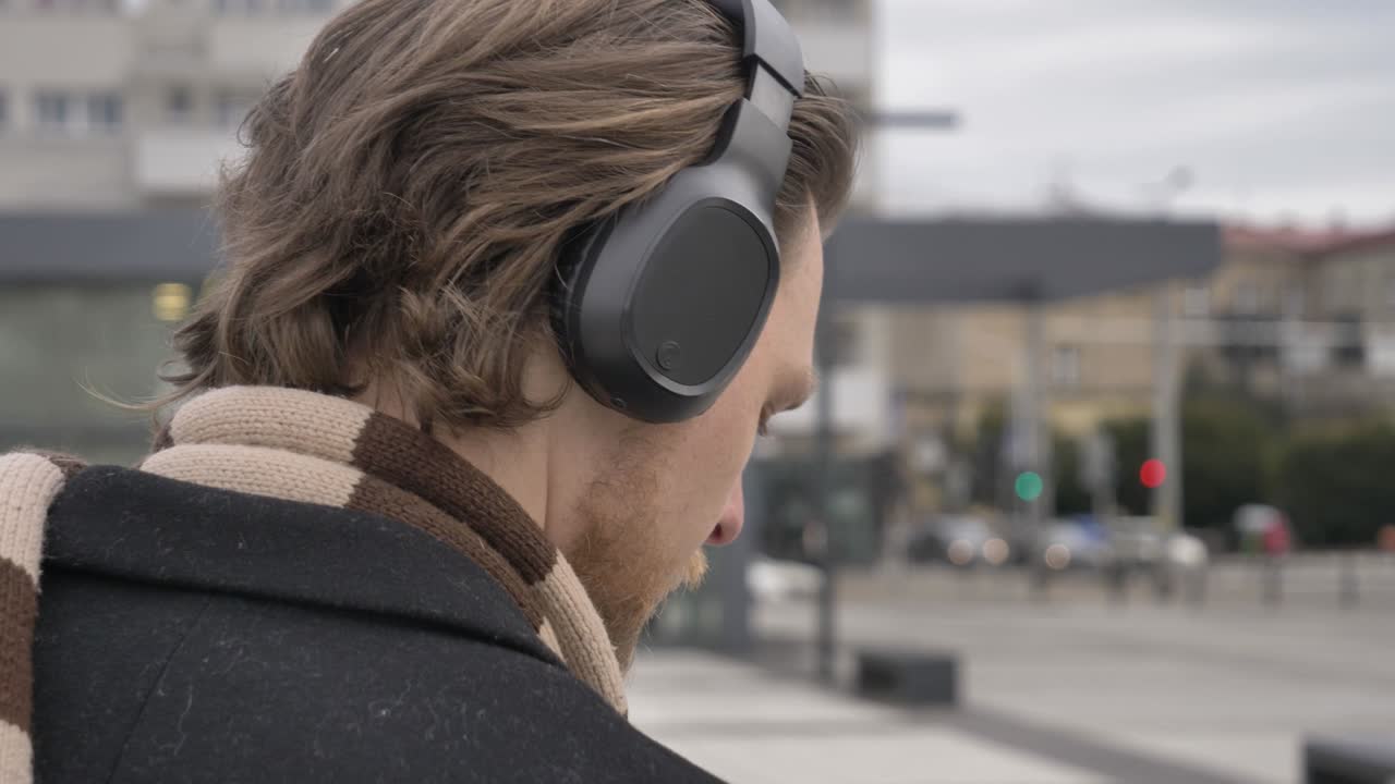 un tipo elegante con bufanda y abrigo escucha música en el servicio de transmisión usando el teléfono móvil