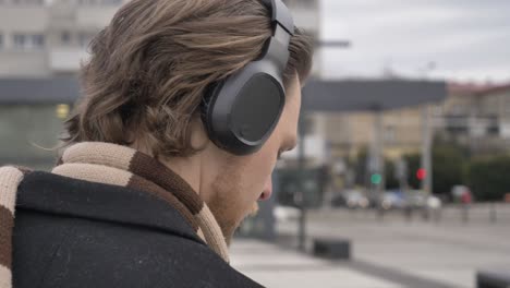 stylish guy in scarf and coat listen a music on streaming service by using mobile phone