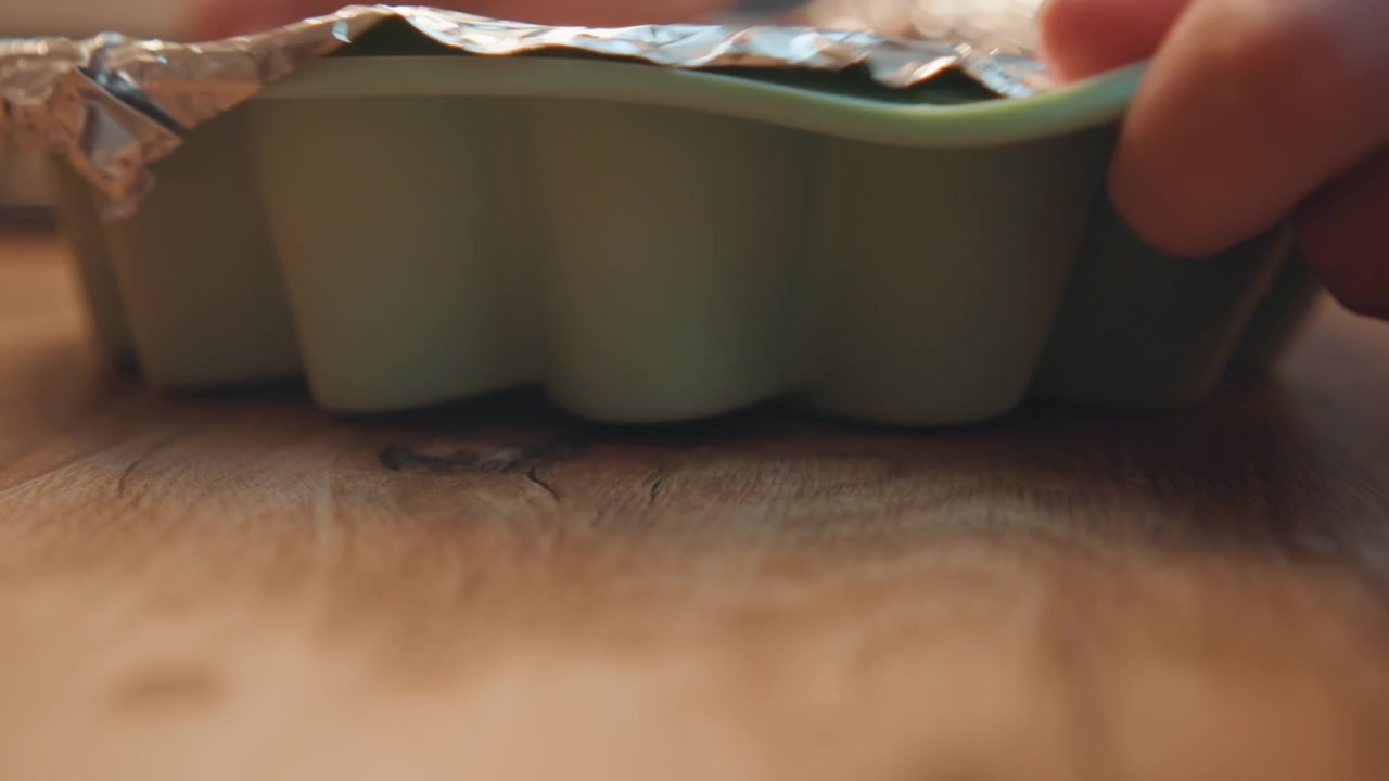 Closeup of baking tray on wooden table. Detailed view of bakery process with baking tools and surface. Detailed depiction of home baker gently pressing silicone mold on wooden surface