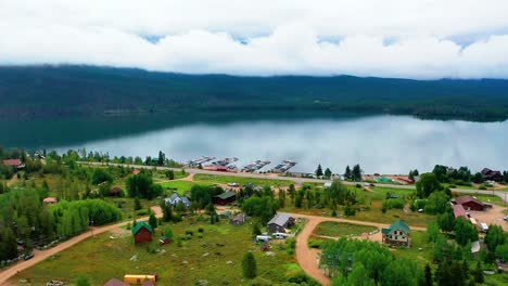 Vista-Aérea-Por-Drones-Del-Hermoso-Lago-De-Montaña-Con-Latas-Rodantes-En-El-Fondo-Y-Aguas-Tranquilas-Y-Reflectantes-De-Vidrio-En-El-Embalse-De-La-Montaña-En-La-Sombra-Y-El-Gran-Lago-A-Lo-Largo-De-La-Costa-Nublada-De-Colorado