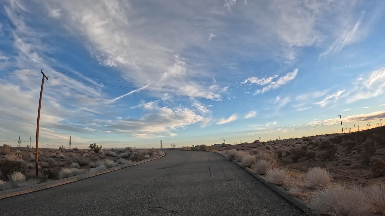 A road leading to a Mojave Desert highway with wispy clouds overhead - cloudscape time lapse