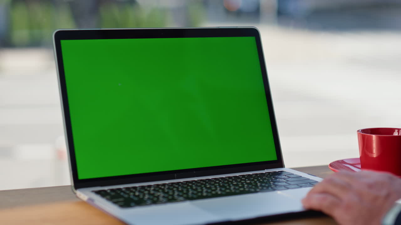 Mano di un uomo che lavora su un mockup di laptop con touchpad, finestre panoramiche e caffetteria in primo piano