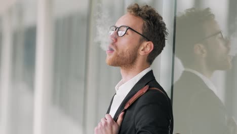 Stylish-young-man-smokes-an-electronic-cigarette-in-the-corridor-of-the-business-center